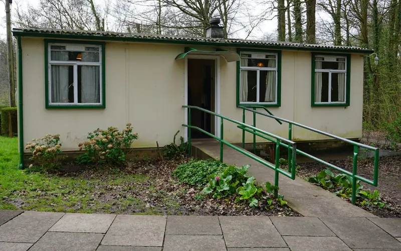 A single-storey cream house with green window frames and a ramp with green handrails leading to the front door